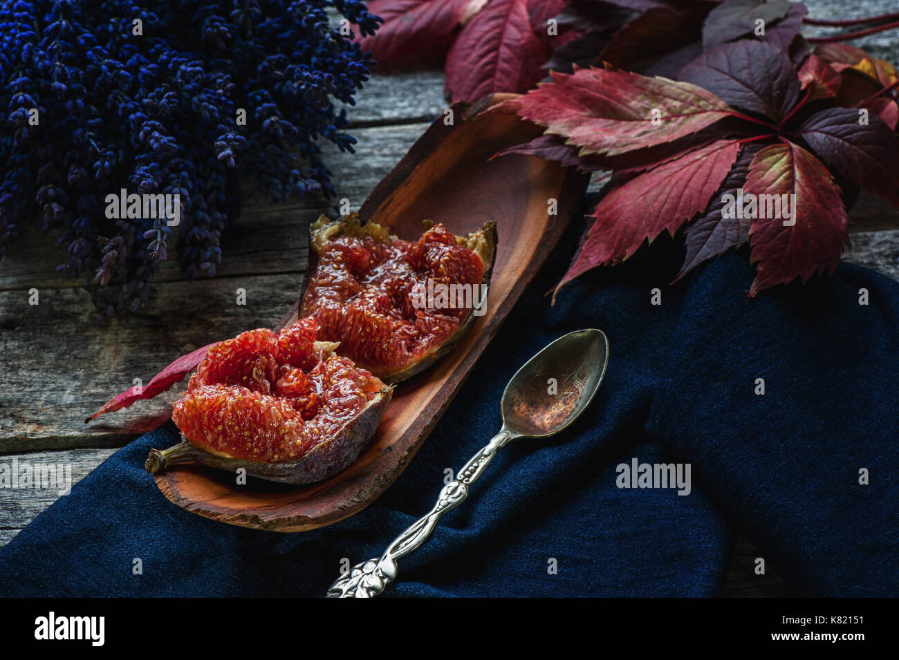Halves of ripe figs with a spoon on a lavender background and a beautiful autumn leaves. Close-up. Rustic. The horizontal frame. Stock Photo