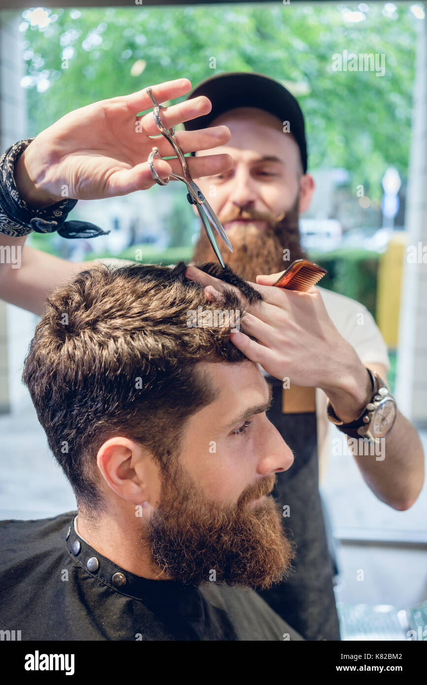 Dedicated hairstylist using scissors and comb while giving a coo Stock ...