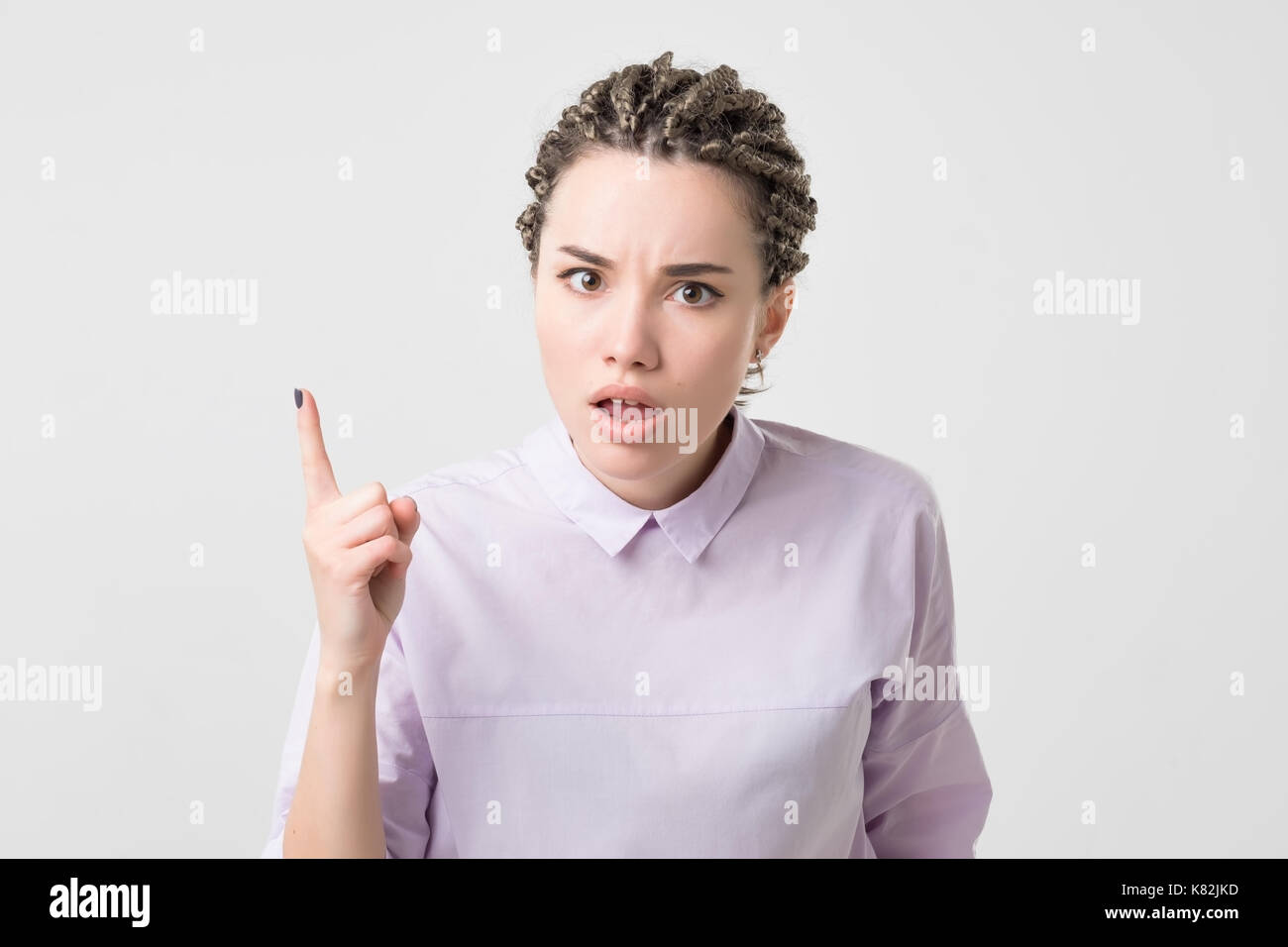 Portrait of serious, frowning, angry, grumpy young woman with african braids pointing finger upwards, scolding someone Stock Photo