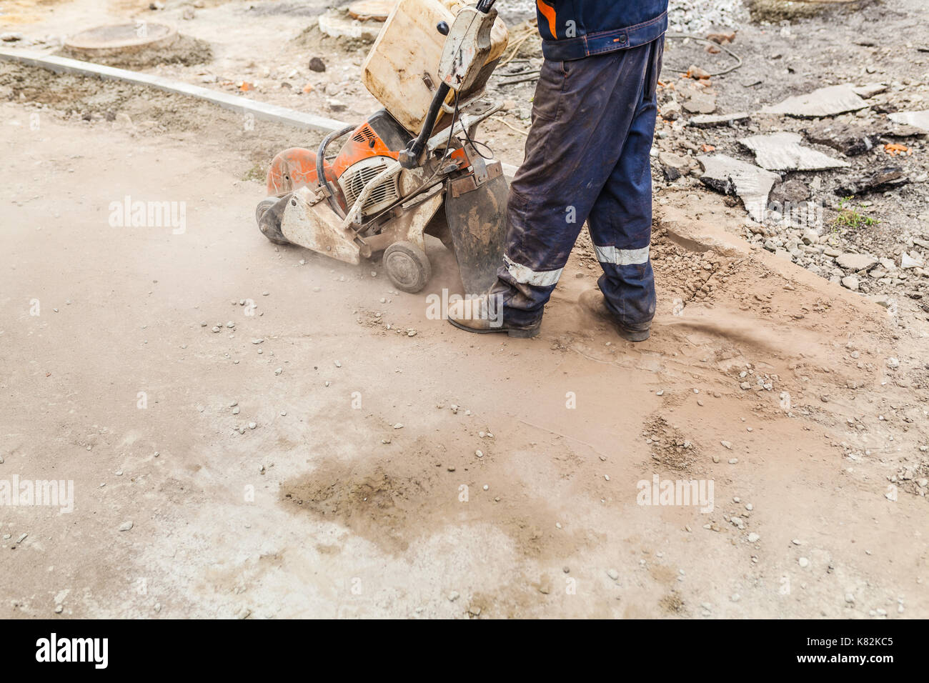 A dirty worker in uniform cutting concrete road with diamond saw blade machine Stock Photo