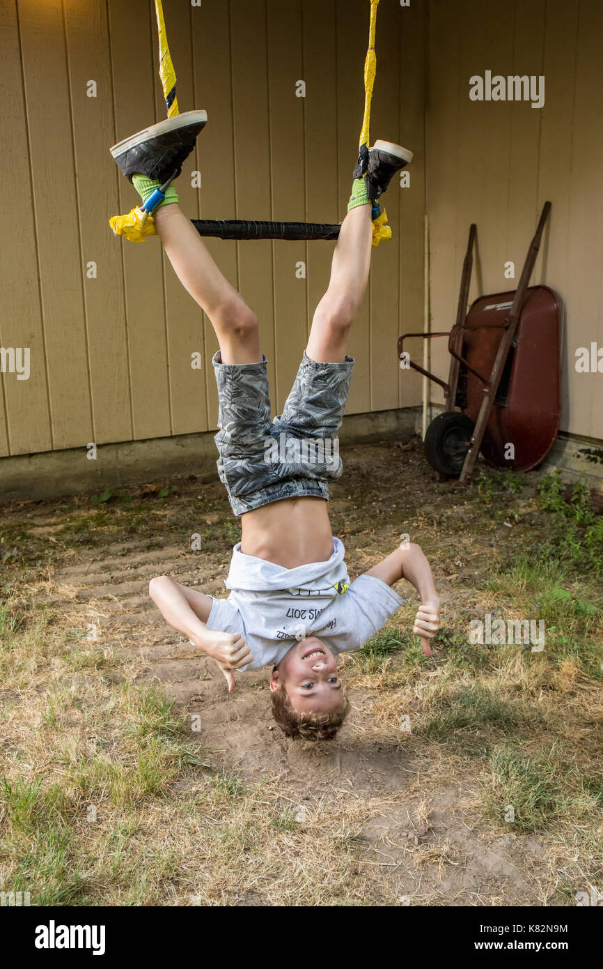 Fourteen year old boy demonstrating his prowess on the trapeze bar in his backyard Stock Photo