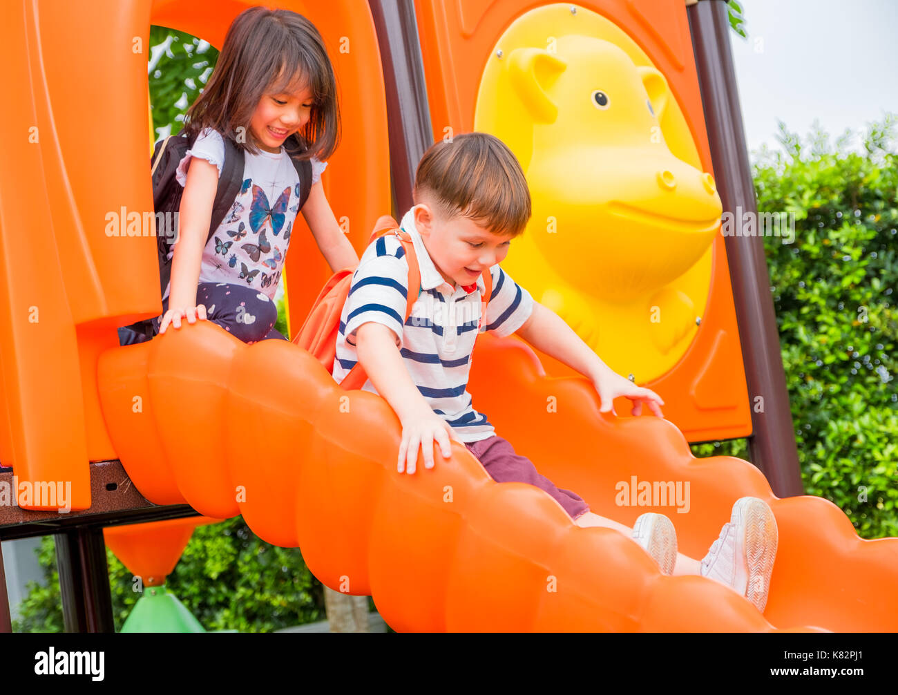 Two kids friends having fun to play together on children's slide at