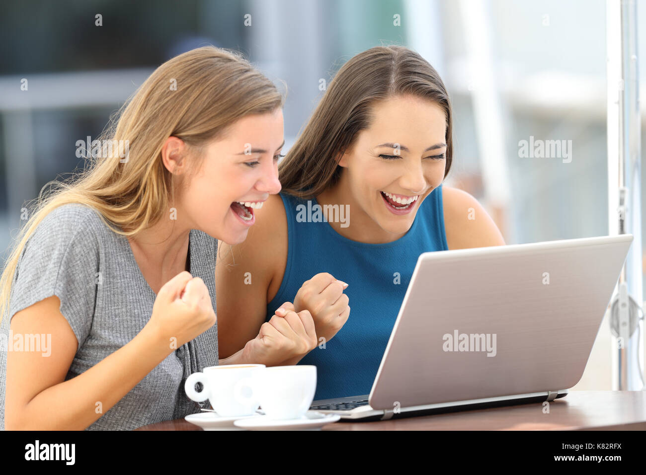 Two excited friends finding on line content in a laptop sitting in a restaurant terrace Stock Photo