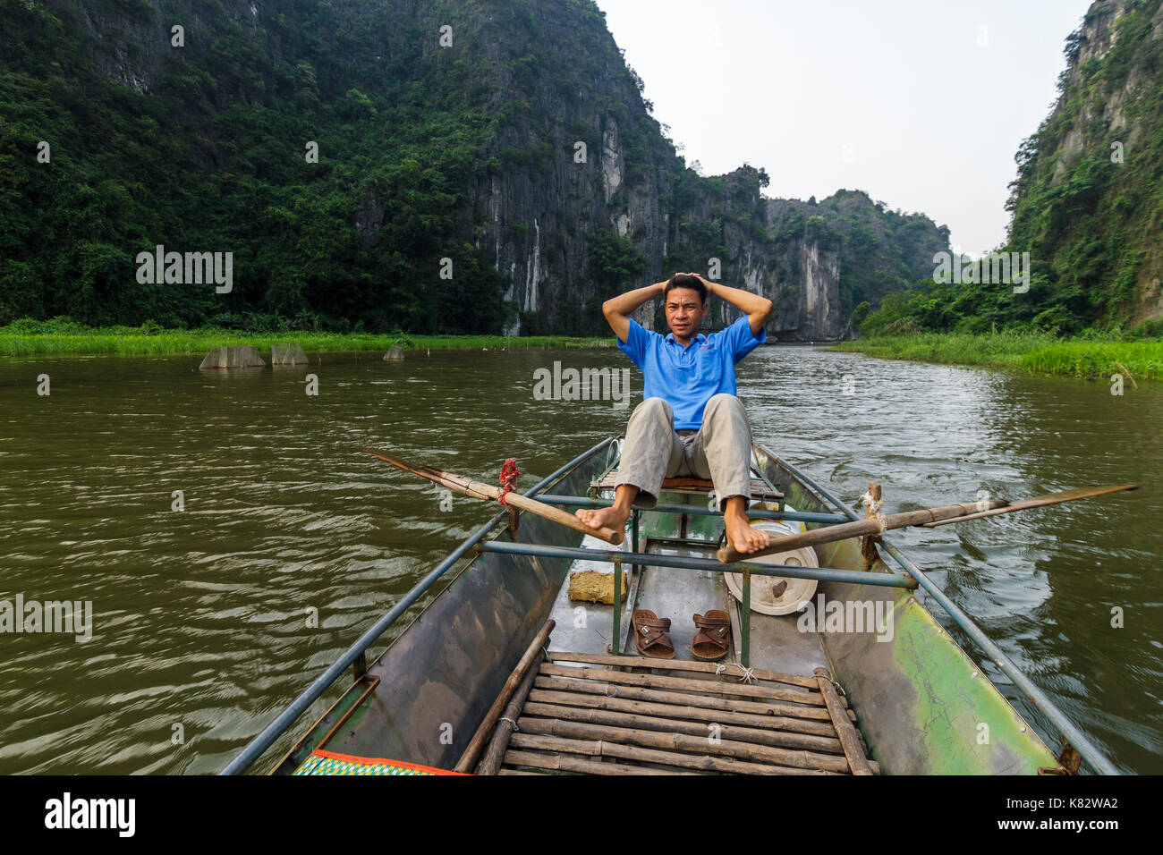 NINH BINH, VIETNAM - 5/6/2016: A tour guide paddles a boat along the Ngo Dong River, near Tam Coc village, at the Trang An UNESCO World Heritage site  Stock Photo