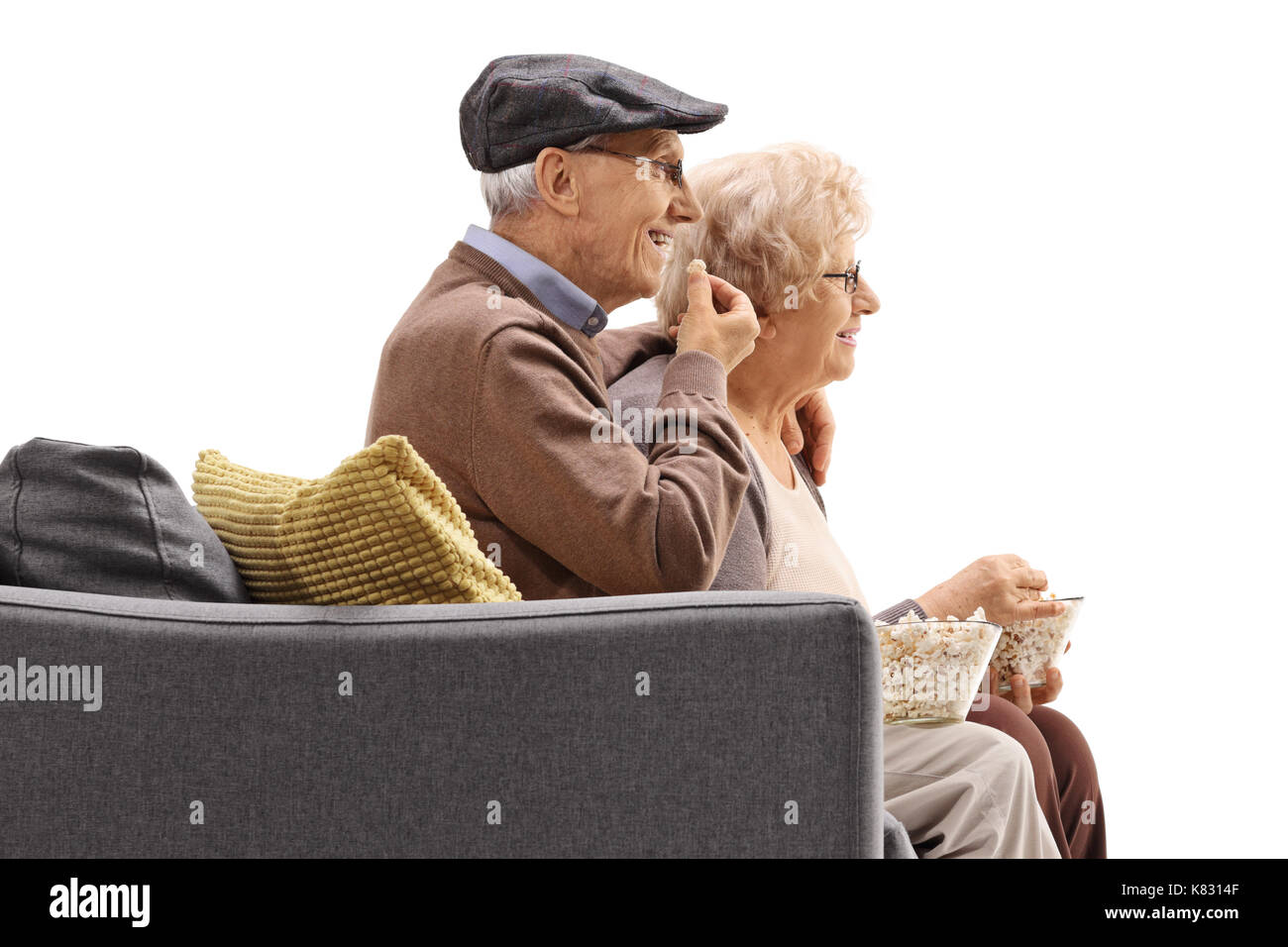 Elderly man and woman sitting on a sofa and eating popcorn isolated on white background Stock Photo