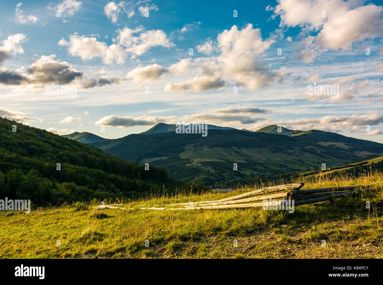 broken wooden fence on grassy hillside in mountains at sunset. landscape with beautiful cloudscape over the ridge Stock Photo