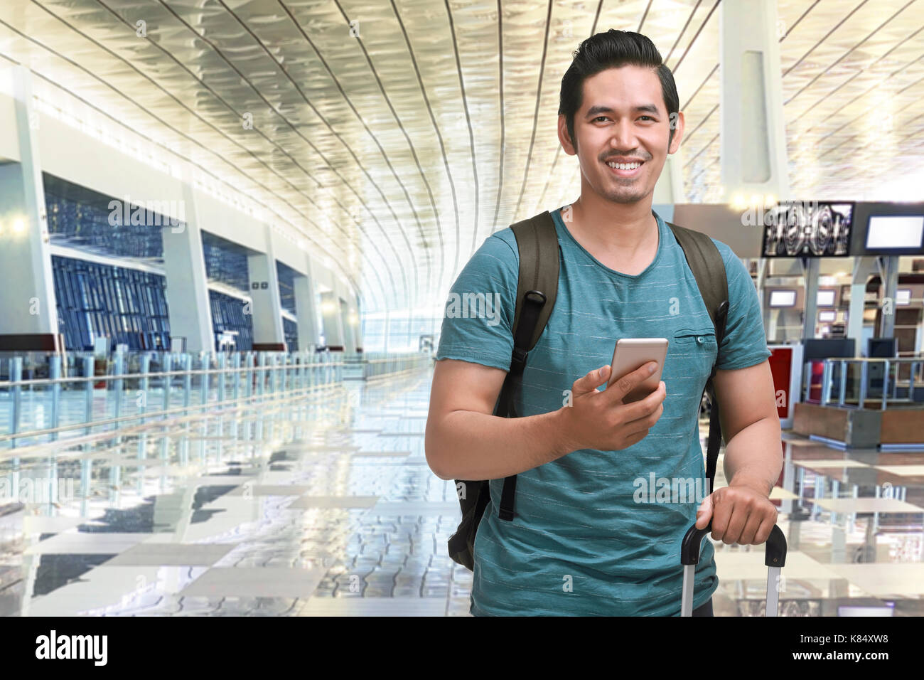 Young asian man traveling with suitcase and mobile phone in airport terminal Stock Photo