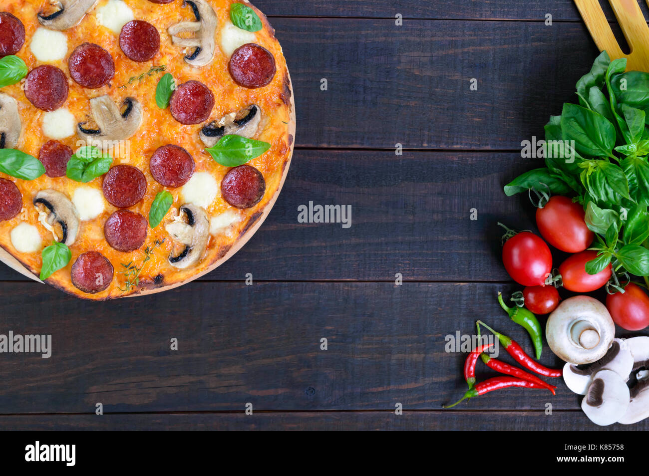 Tasty Italian pizza with salami, mushrooms, mozzarella, basil on a dark wooden table. Top view. Stock Photo