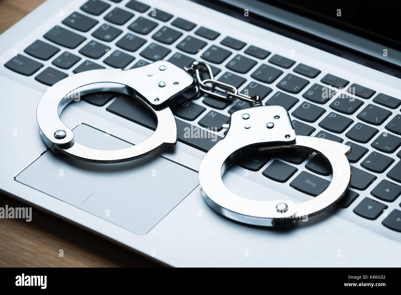 Closeup of handcuffs on laptop at table Stock Photo