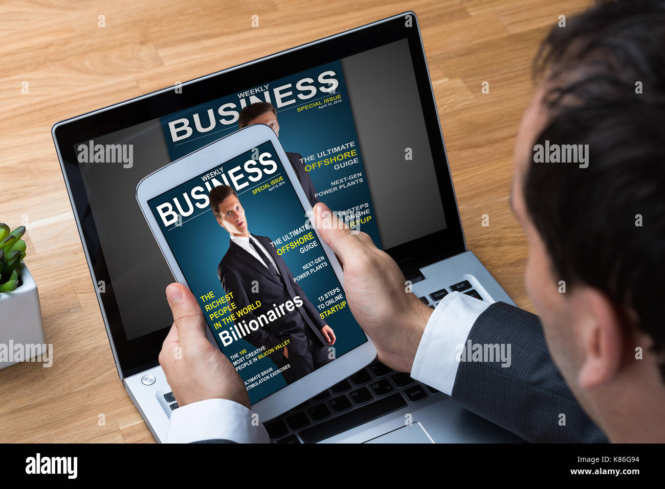 Cropped image of businessman reading business magazine on tablet and laptop in office Stock Photo