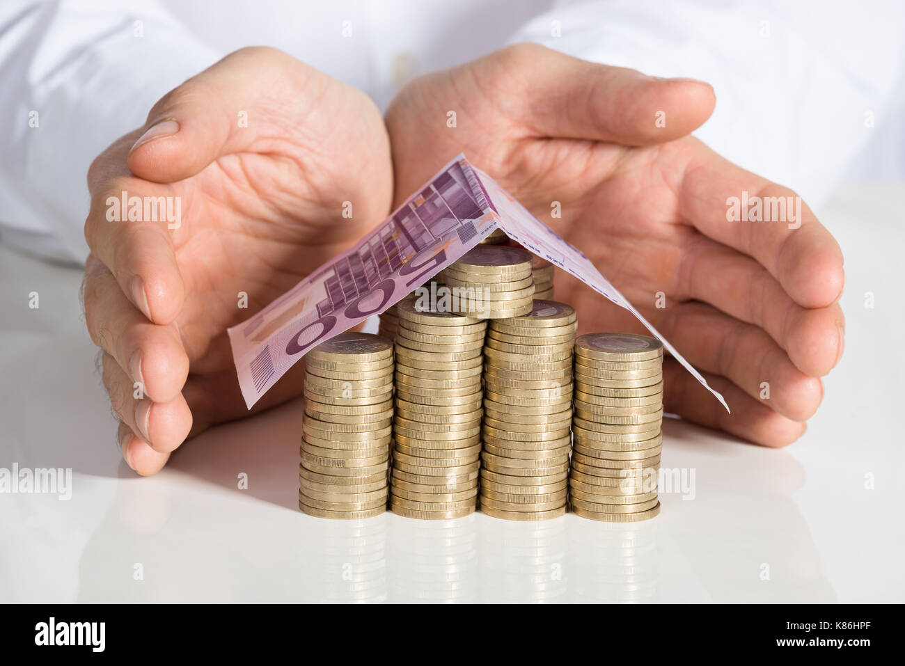 Midsection of businessman protecting house made from coins and banknote at office desk Stock Photo