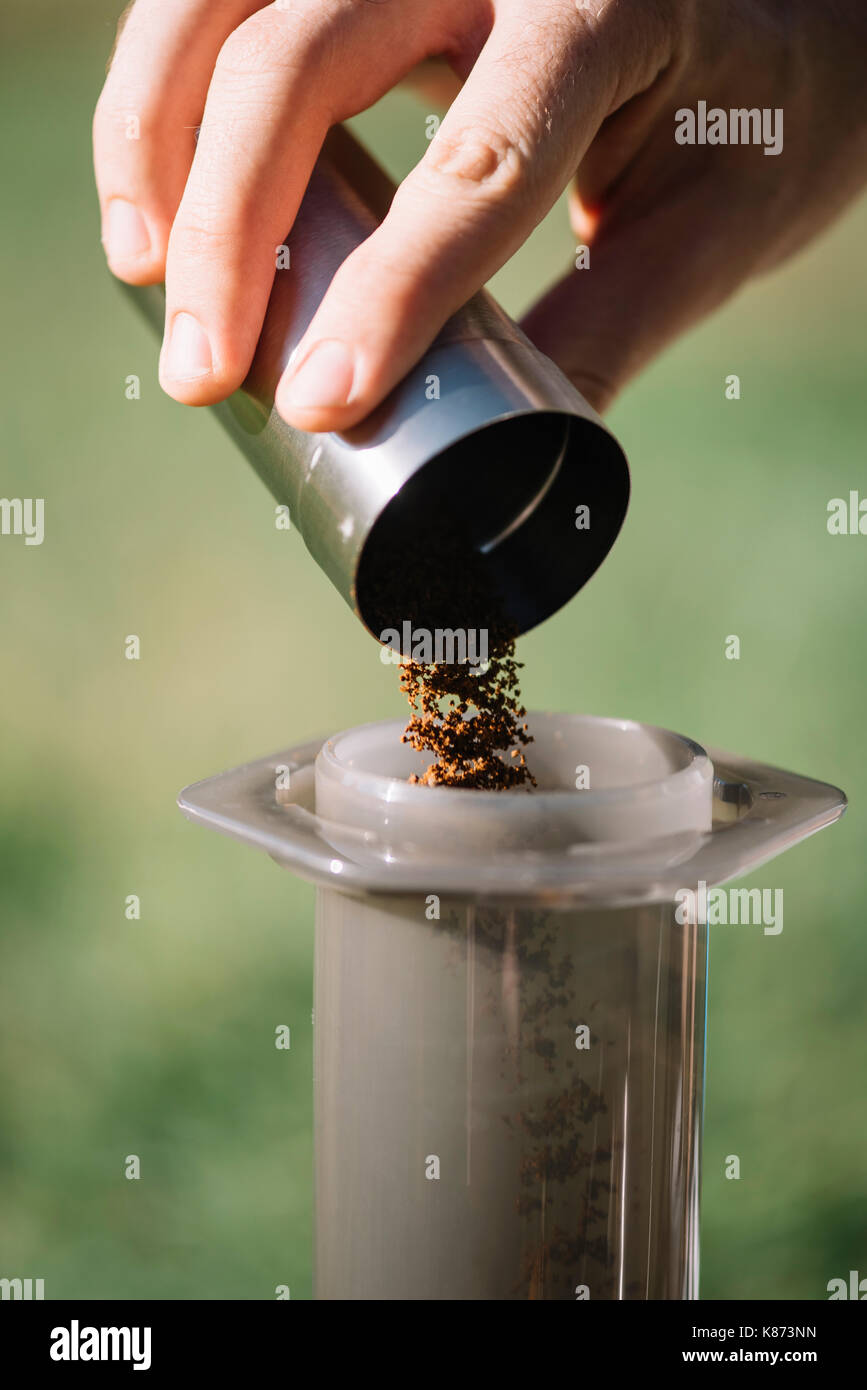 Delicious freshly ground morning coffee beans being thrown into manual coffee grinder, close up view. process of making coffee Stock Photo