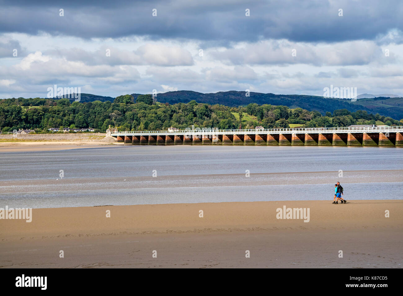 Two People Walking on the Sands Below Arnside Viaduct as the Tide Recedes, Arnside, Cumbria, UK Stock Photo