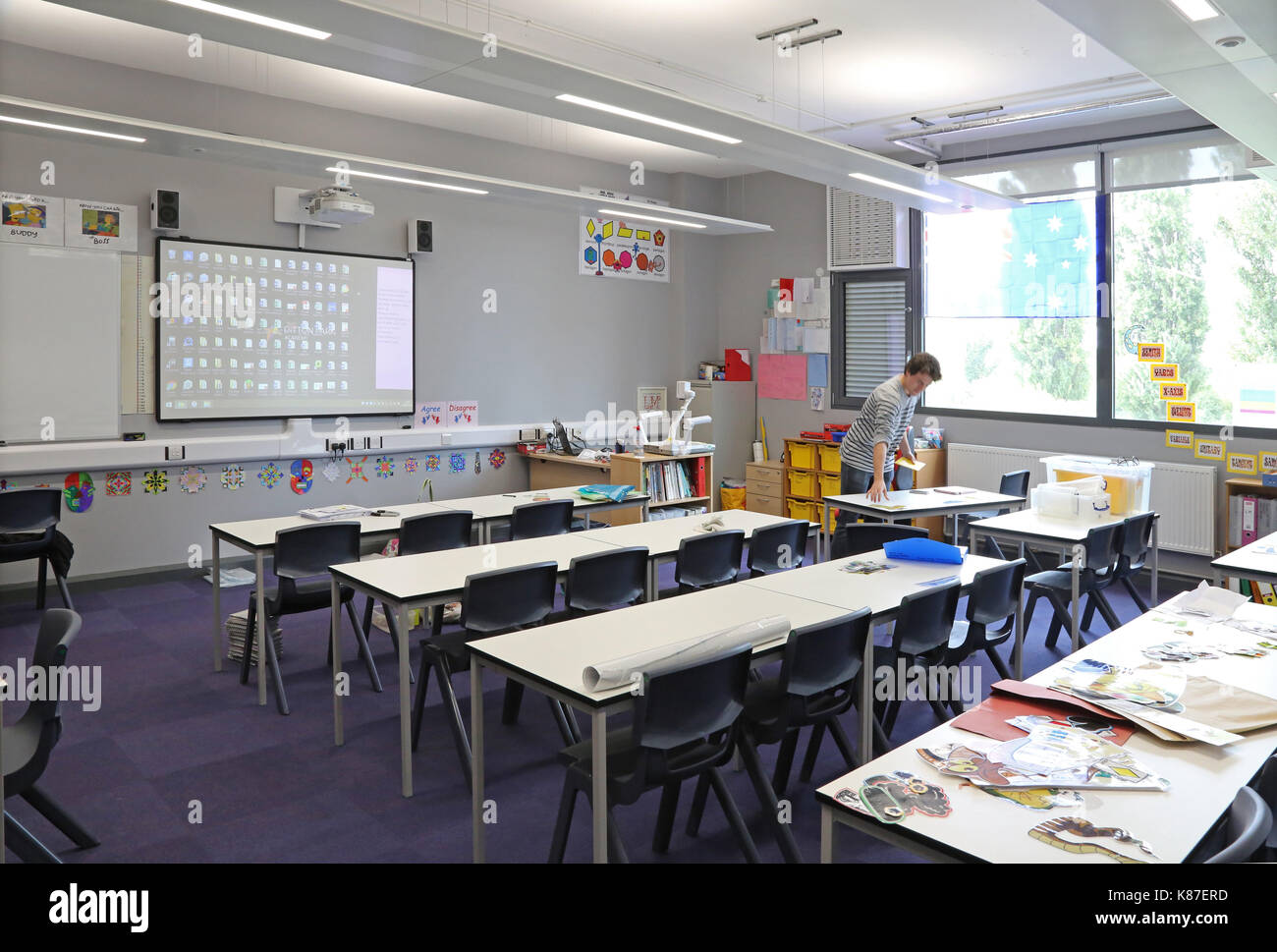 A teacher works alone in a modern classroom in a new London secondary school. Traditional layout with desks facing a large monitor screen. Stock Photo