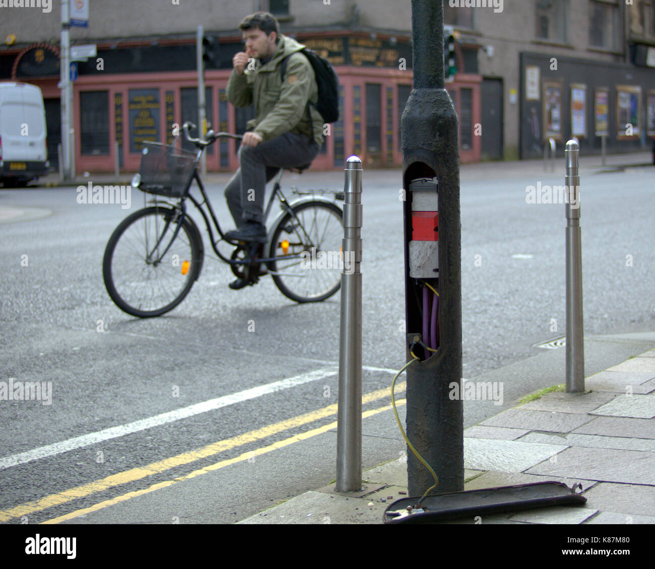 cyclist  on in Glasgow bike cycles past vandalized opened lamppost with cables showing  a comment on Lamp post charging being considered in Scotland Stock Photo