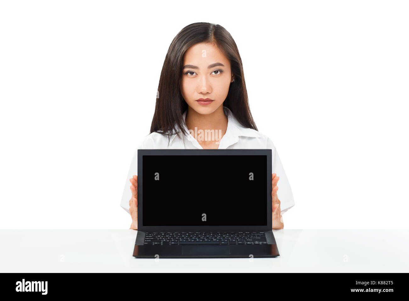 Serious Asian young woman sitting at table with laptop. Black netbook ...