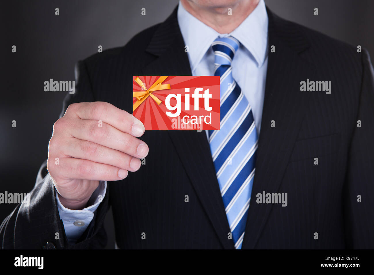 Close-up Of Businessman Holding Gift Card Over Black Background Stock Photo