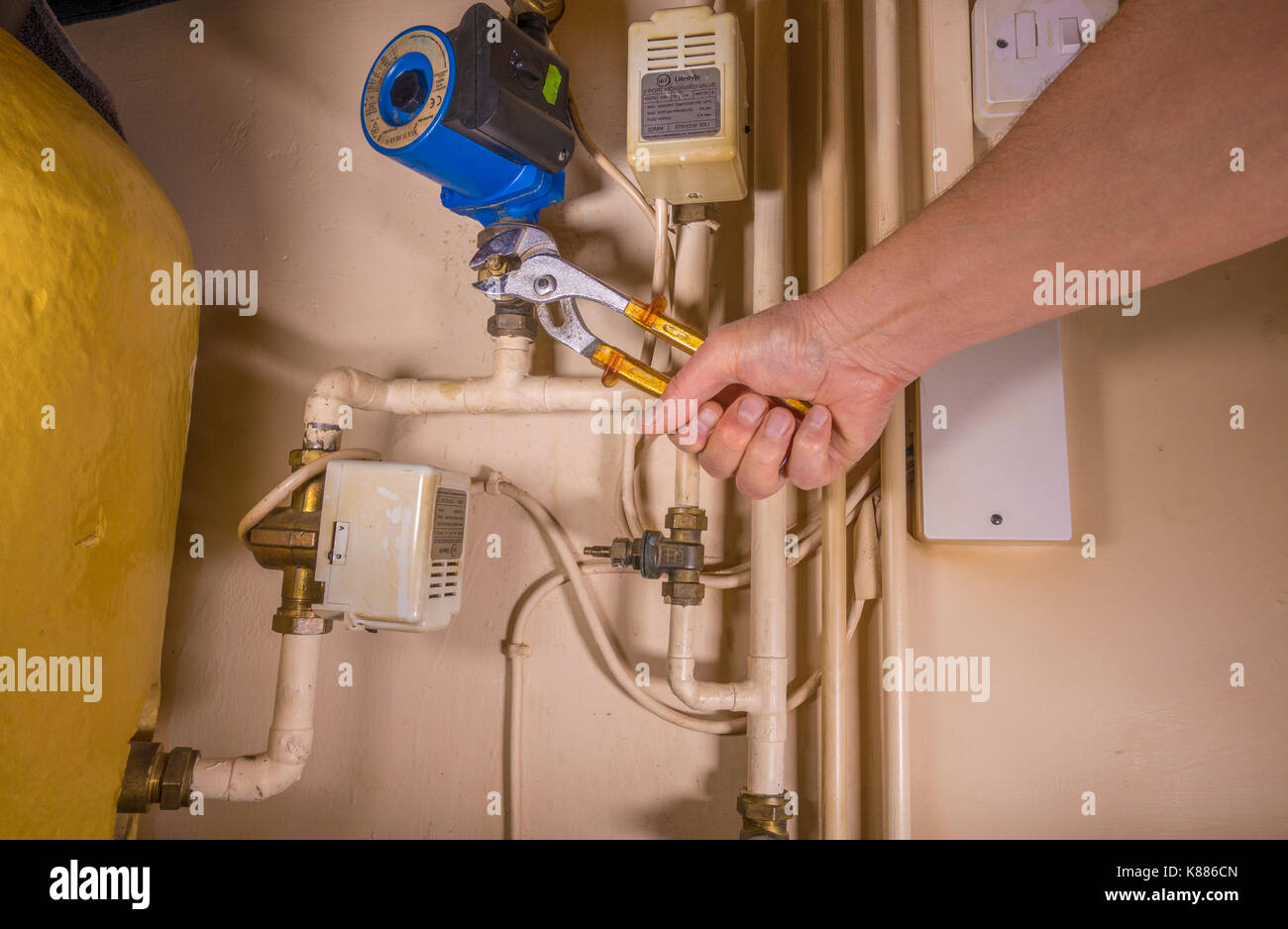 A plumber working in an airing cupboard, using an adjustable wrench to work on a defective central heating pump. England, UK. Stock Photo