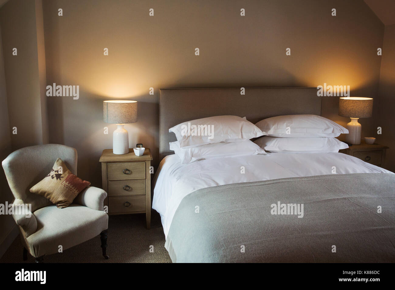 A cosy bedroom decorated in neutral colours, with a double bed and bedside lights on. Hospitality. Stock Photo