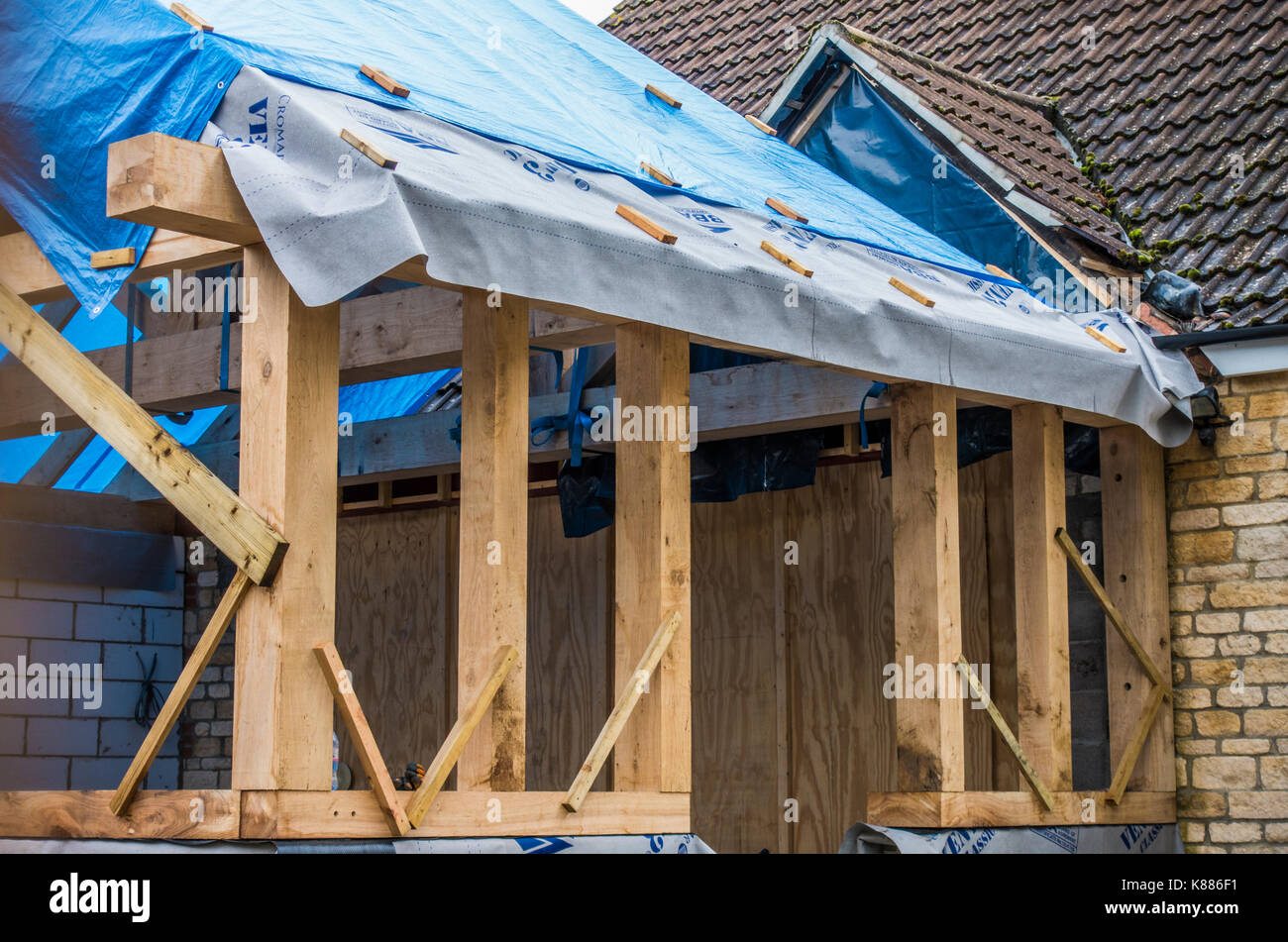 A house extension undergoing construction, with a substantial wooden structure and protective covering over the pitched roof timbers. England, UK. Stock Photo