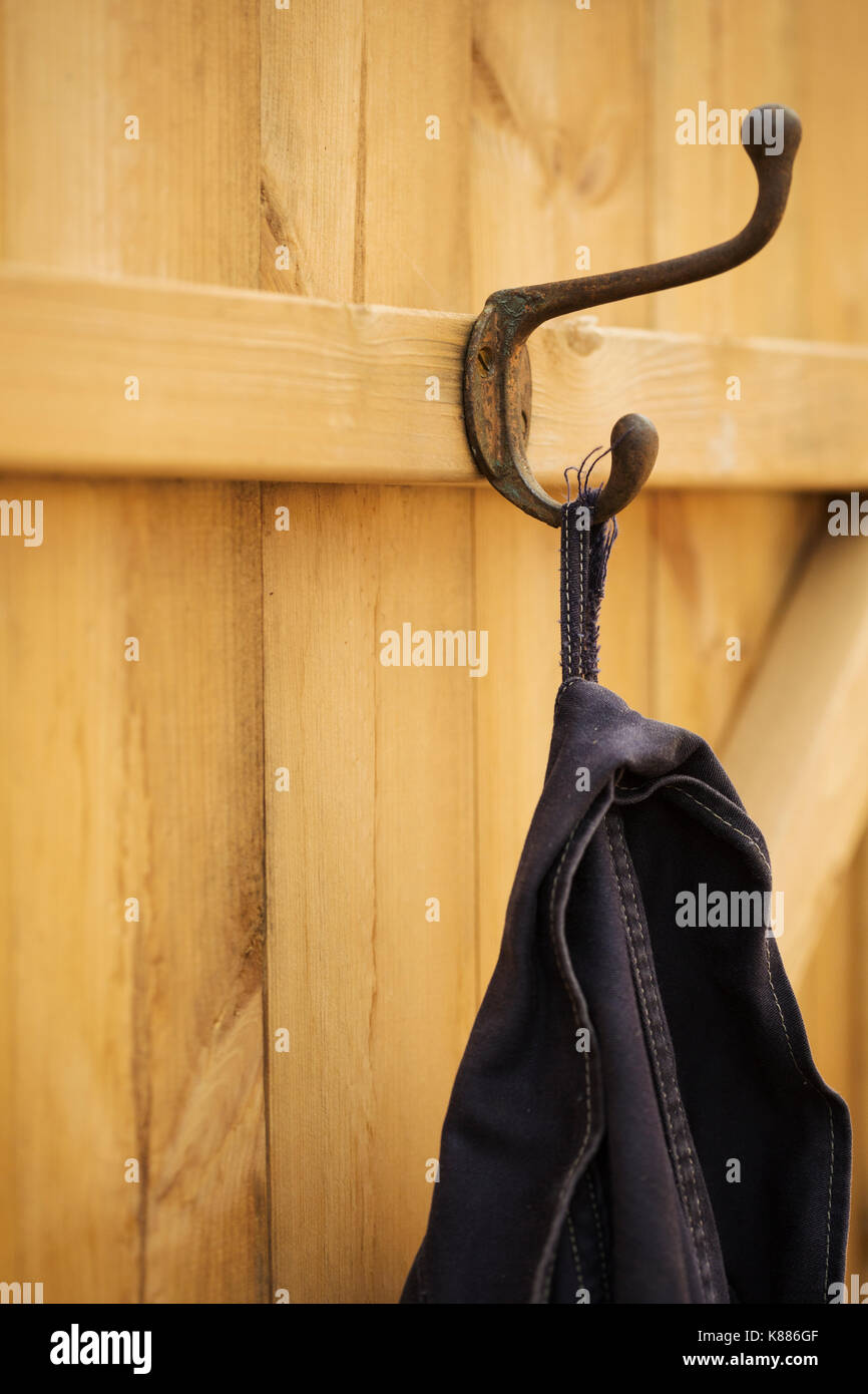 A black jacket hanging from a metal coathook on the back of a wooden door. Stock Photo