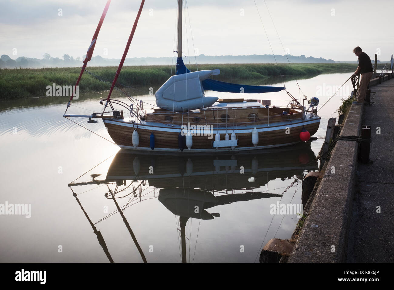 Man standing on side of harbour wall, casting off a sailing boat into the river. Stock Photo