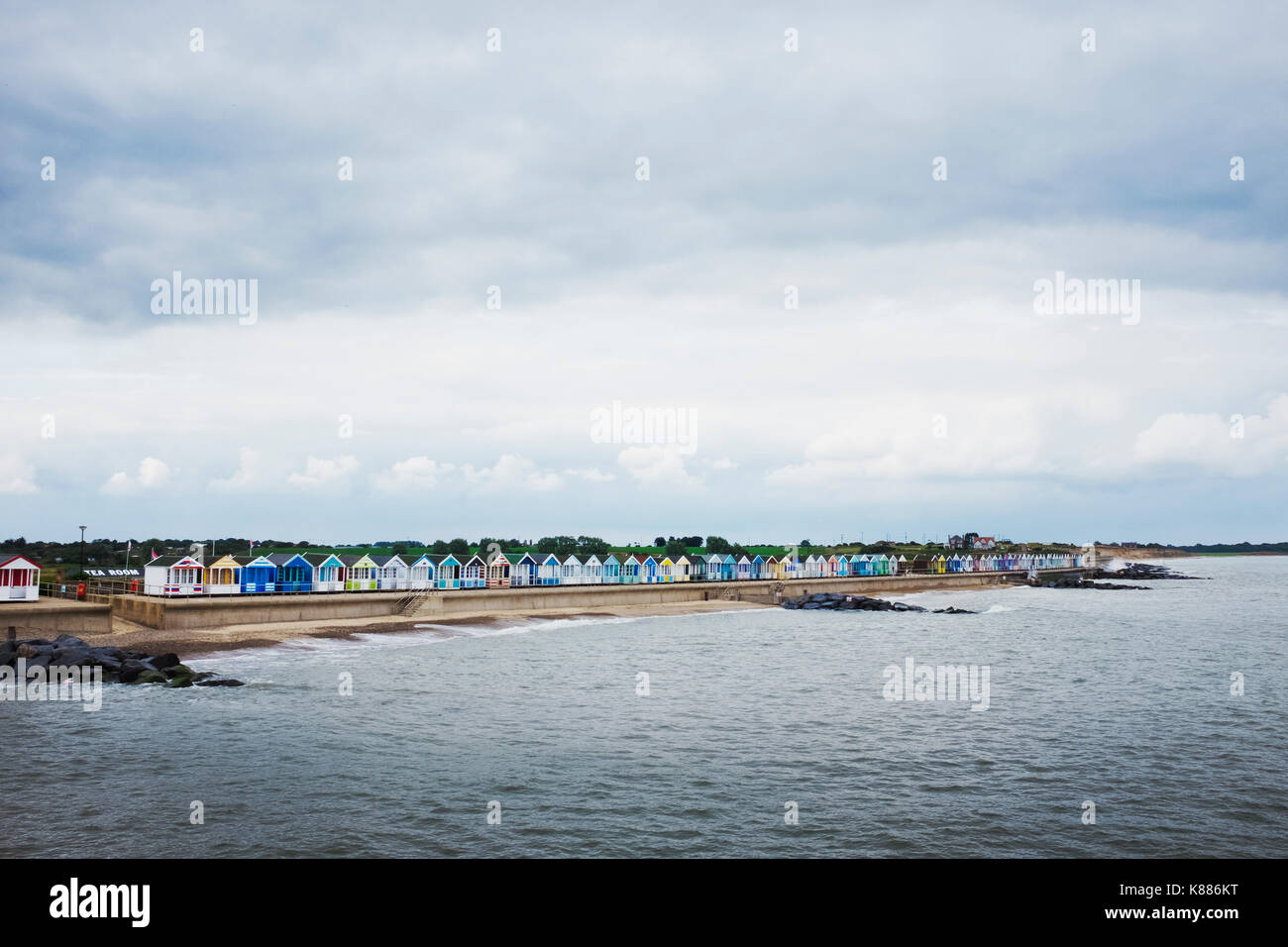 Long row of painted beach huts on a sandy beach overlooking the water. Stock Photo