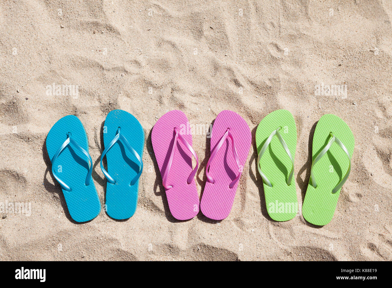 Three Pairs Of Flip-flops In A Row On Beach Stock Photo