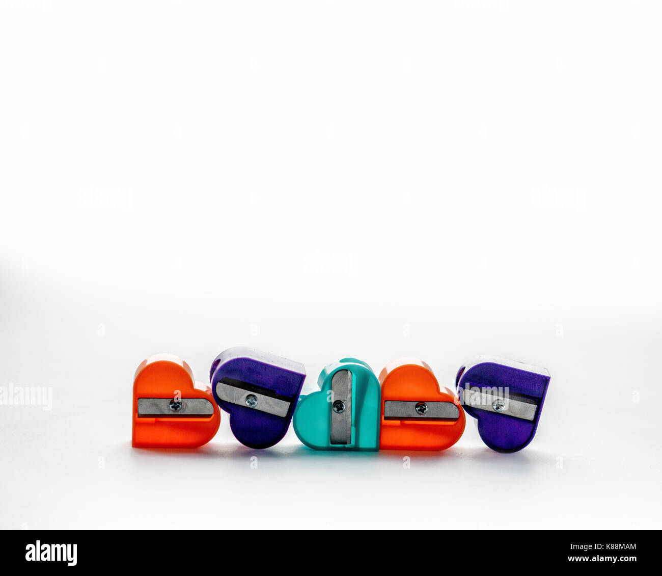 Five colorful pencil sharpeners in the shape of a heart on the white background. Front view. Stock Photo