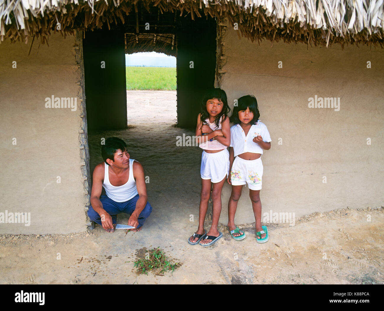 A father and his two daughters, Pemon Indians, in a work shed in a small, remote rainforest village in the Gran Sabana region of Venezuela near Angel  Stock Photo