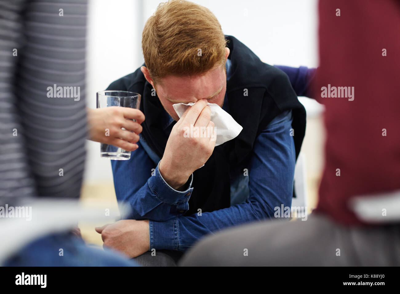 Frustrated man crying while one of his friends offering him glass of water Stock Photo
