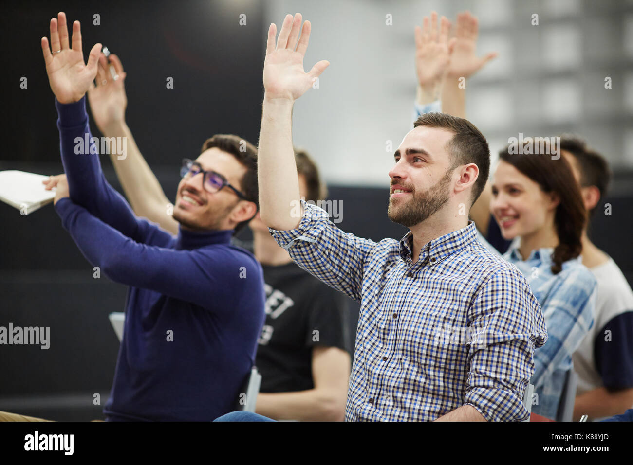 Clever business course learners raising hands to answer questions of teacher or making suggestion during discussion Stock Photo