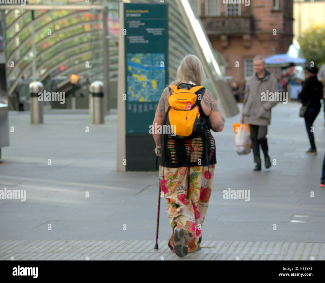 older trendy woman with walking stick colorful walking on street st Enoch square Stock Photo