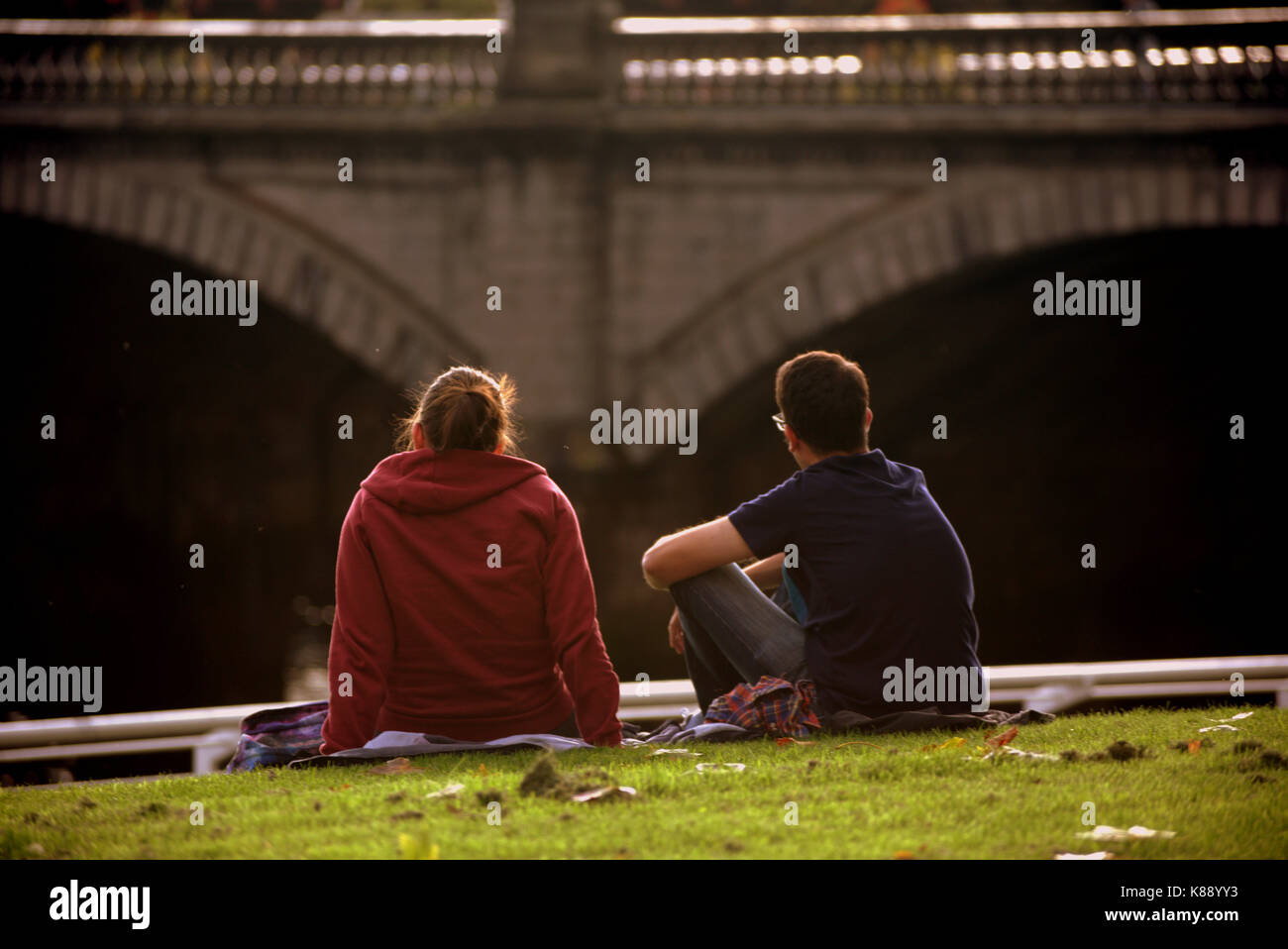 tourist couples sit on the grass on the banks of the Clyde river Glasgow Scotland Stock Photo