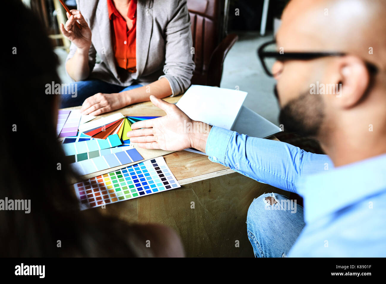 One of designers pointing at variety of colors in palette while consulting with colleagues Stock Photo
