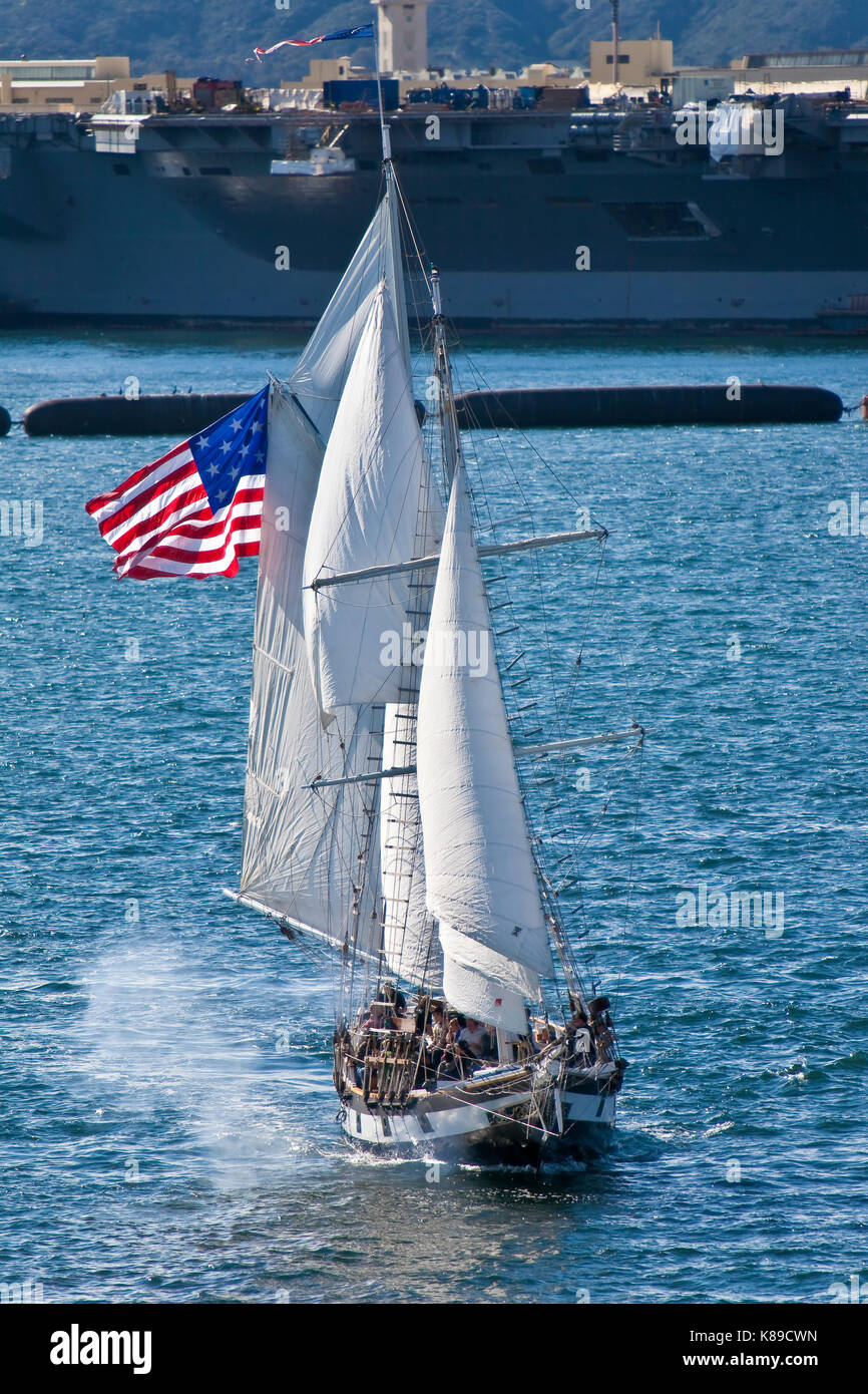 Tall Sailing Ship Anazing Grace under full sail on San Diego Bay, CA US fires cannons during naval battle with aircraft carrier in background  Amazing Stock Photo