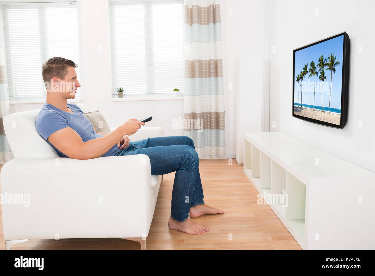 Young Man Sitting On Sofa Watching Television At Home Stock Photo
