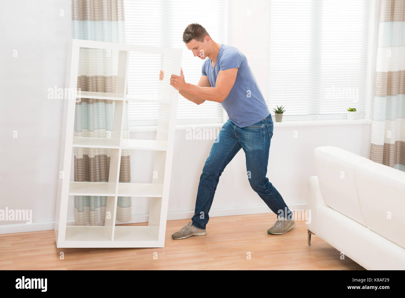 Человек передвигает шкаф. Ремни для переноски мебели. Тяжелый шкаф. Передвигать мебель. Передвинуть тяжелую мебель.