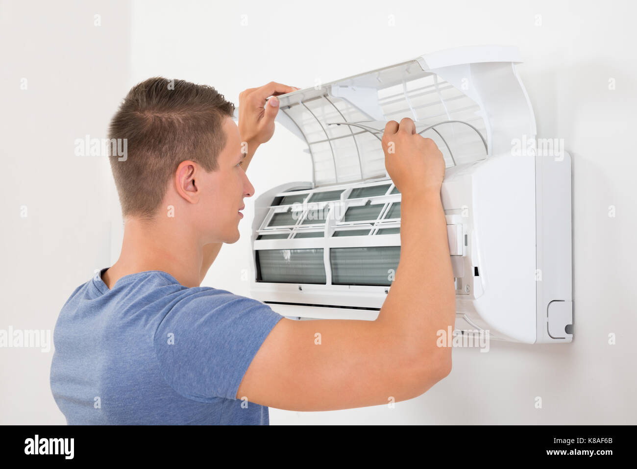 Young Man Checking Air Conditioner Mounted On White Wall Stock Photo