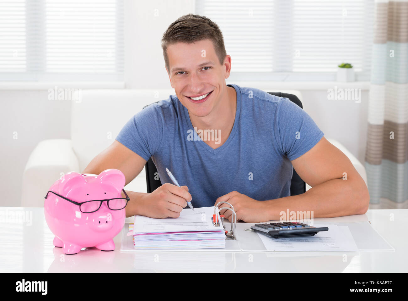 Happy Man With Piggybank Calculating Receipt At Desk Stock Photo - Alamy
