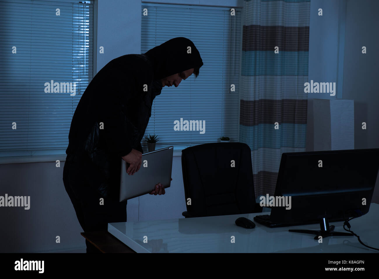 Male Thief Stealing Laptop From Office At Night Stock Photo