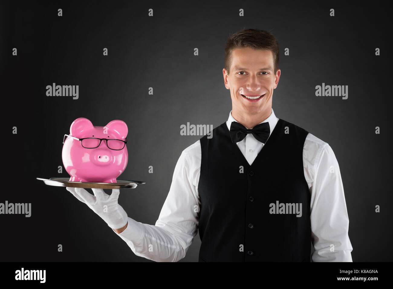 Portrait Of Happy Butler Holding Tray With Pink Piggybank Stock Photo