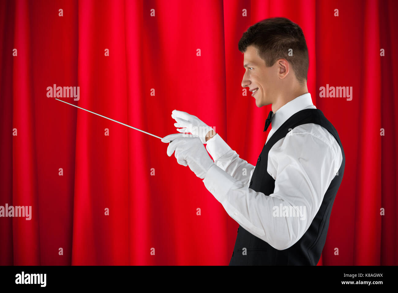 Male Orchestra Conductor Holding Baton Over Red Curtain Stock Photo