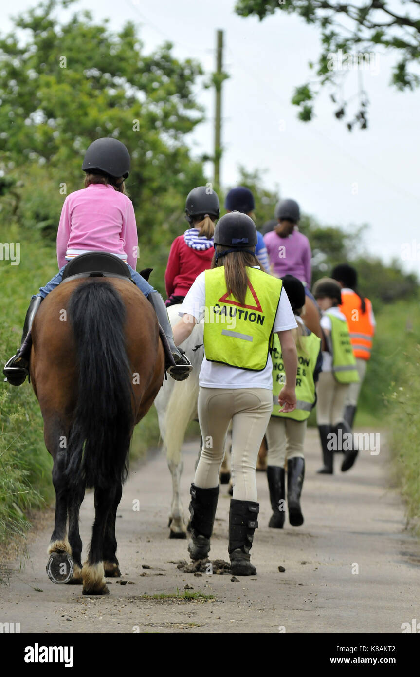 A group of horse riders pony trekking through some green and lush woodland wearing high visibility vests for safety when riding a horse on the road. Stock Photo