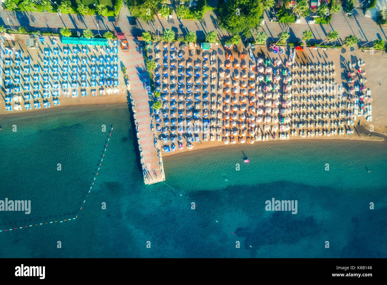 Aerial view of transparent turquoise sea, beautiful sandy beach with colorful chaise-lounges, boats, green trees, hotels, buildings at sunrise in Icme Stock Photo
