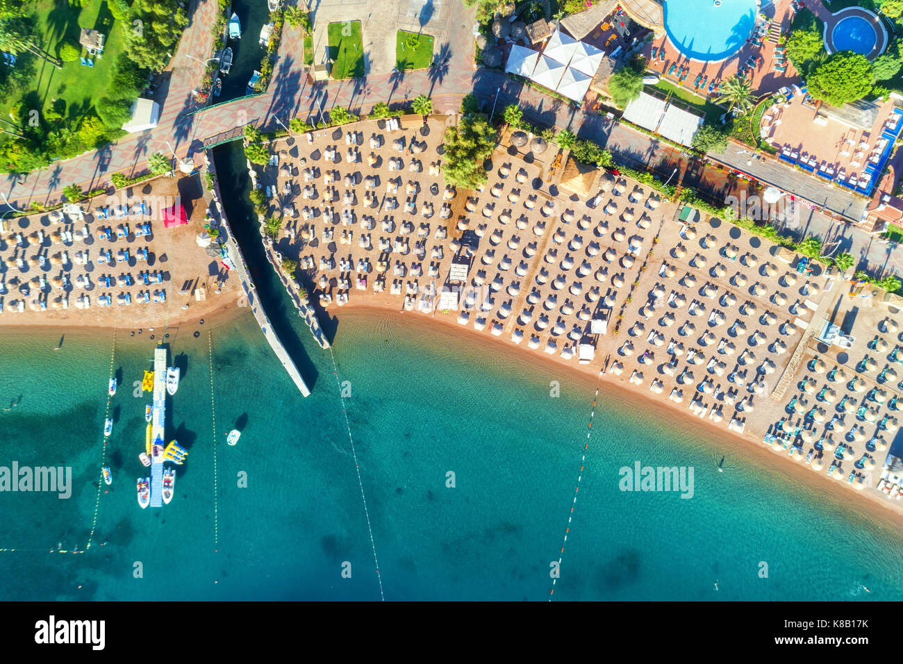 Aerial view of transparent turquoise sea, beautiful sandy beach with colorful chaise-lounges, boats, green trees, pool, hotels, buildings at sunrise i Stock Photo