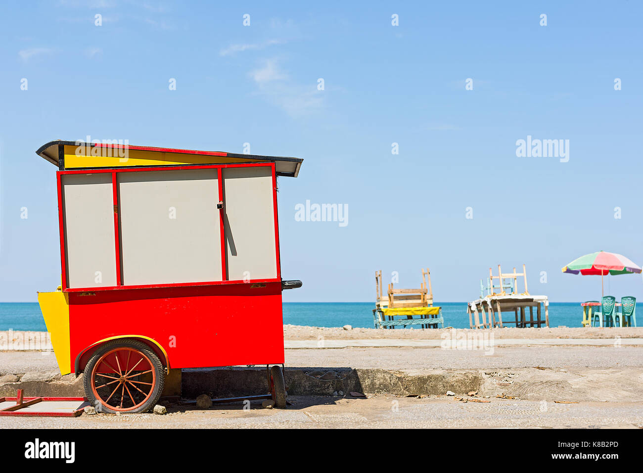 A street vendors cart all closed up at the beach side promenade during the day with basic stacked table and chairs in the background. Stock Photo