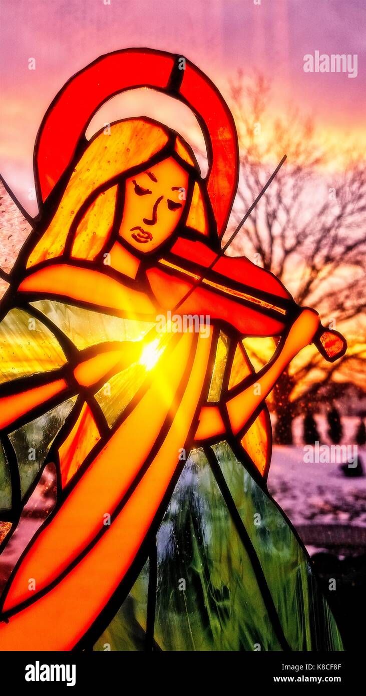 An angel playing the violin. Stained glass angel. Winter background. Colorful scenery. Sun shining through the stained glass. Stock Photo