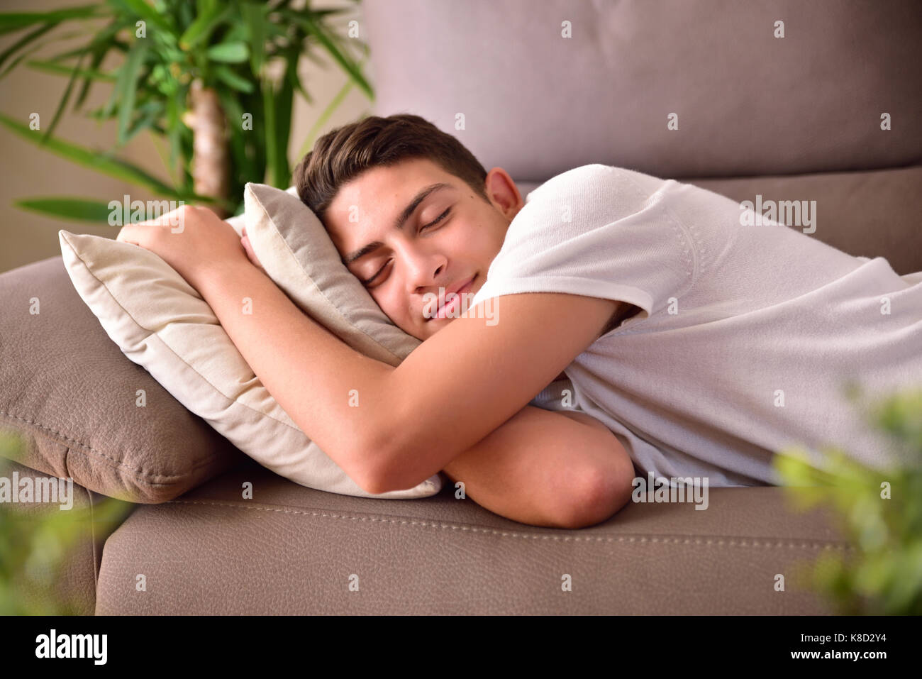 Man napping happily lying on a couch clinging to cushions at home. Front view Stock Photo