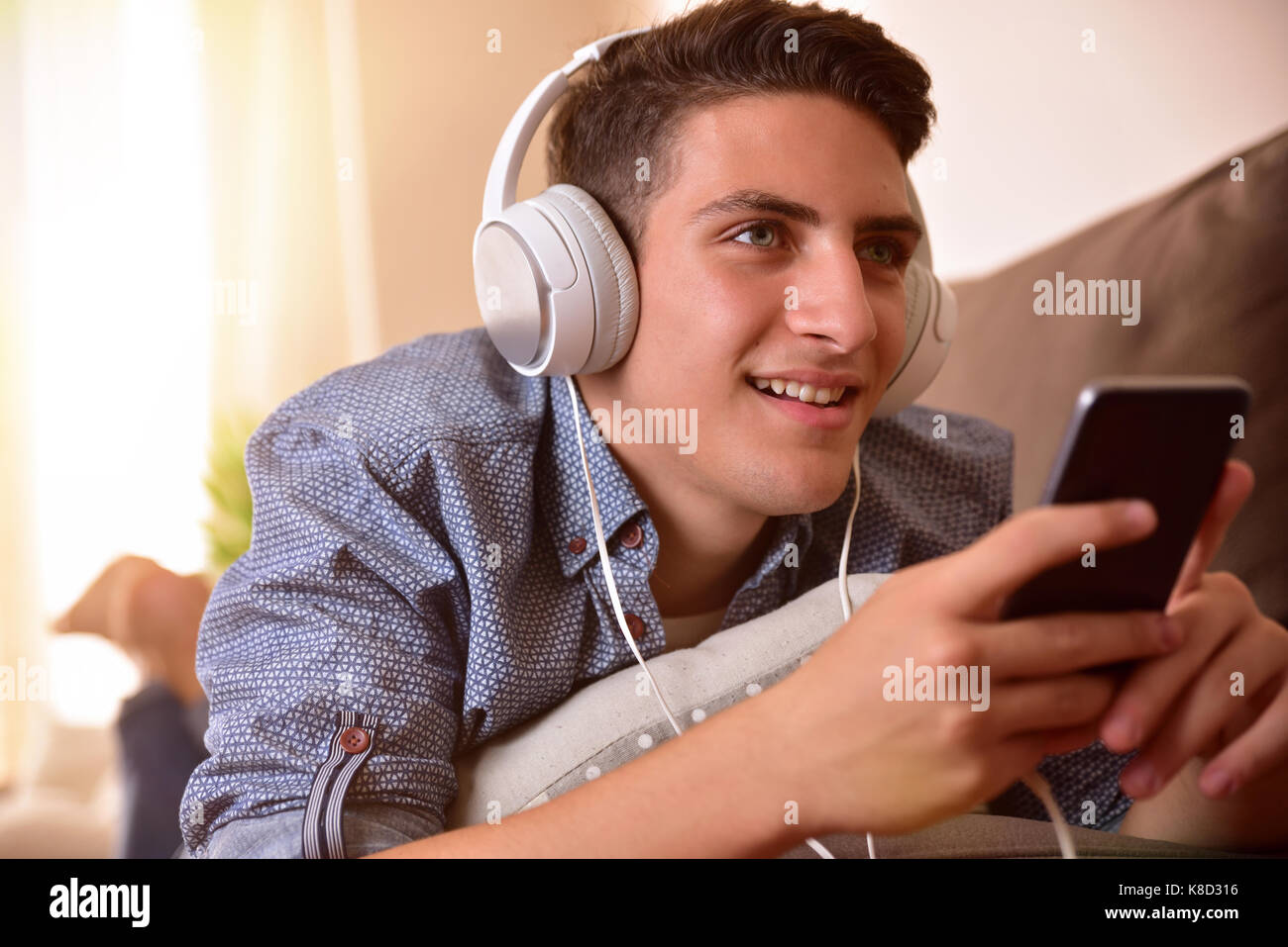 Teen listening music with headphones from mobile lying face down on couch Stock Photo